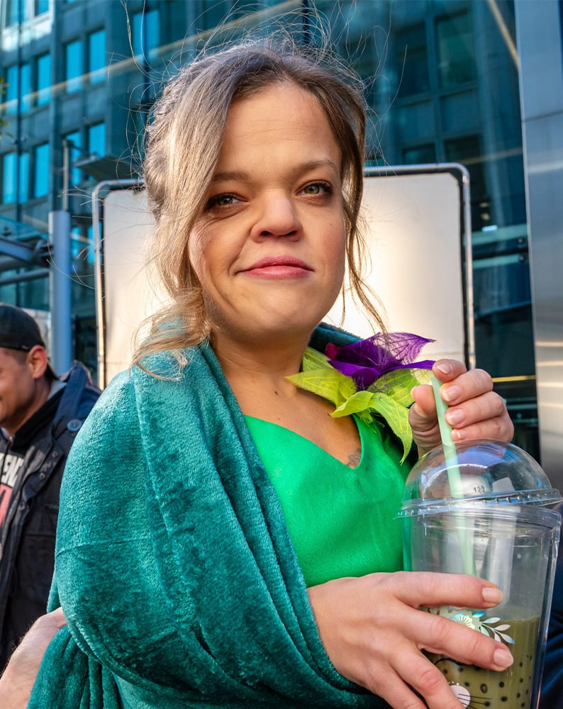Zdjęcie Ani z planu filmowego. Ania patrzy prosto w kamerę, w ręku trzyma plastikowy kubek z bubble-tea i wystającą zieloną słomką.