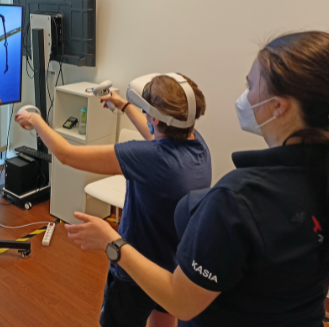 Na zdjęciu pacjentka podczas zajęć w VR i asekurująca ją fizjoterapeutka.