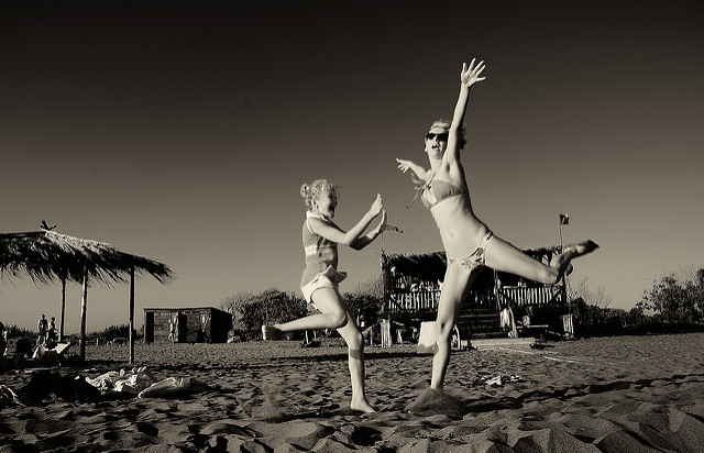 Dwie kobiety na plaży podskakują z uniesionymi rękami