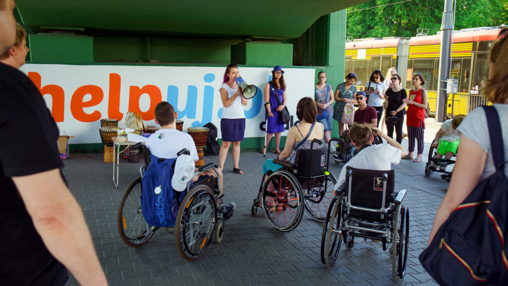 Zdjęcie z otwarcia wernisarzu muralu Helpuj.pl - grupa uczestników pod muralem. Osoby na wózkach i pełnosprawne.