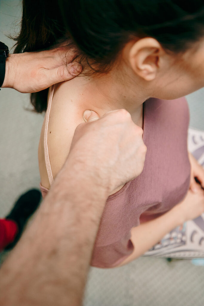 Na zdjęciu zbliżenie na ramię pacjentki uciskane przez fizjoterapeutę.