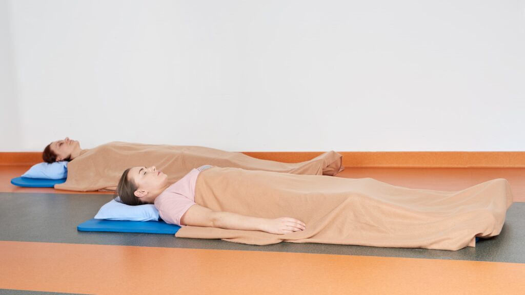 Trenerka i pacjentka podczas zajęć relaksacyjnych - leżą na podłodze przykryte kocami.