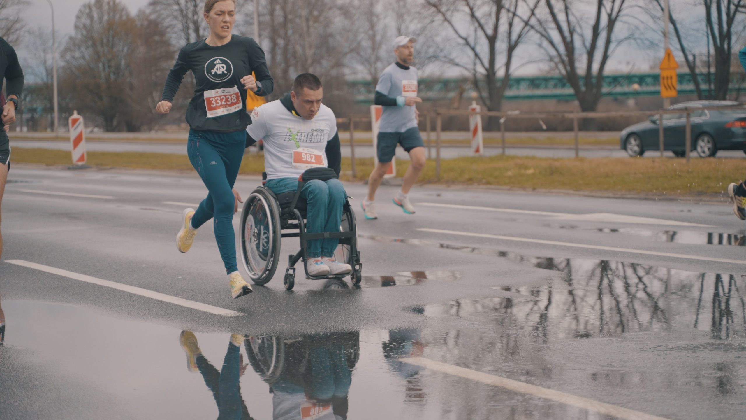 Trzy osoby biegną w maratonie, w tym jedna na wózku.
