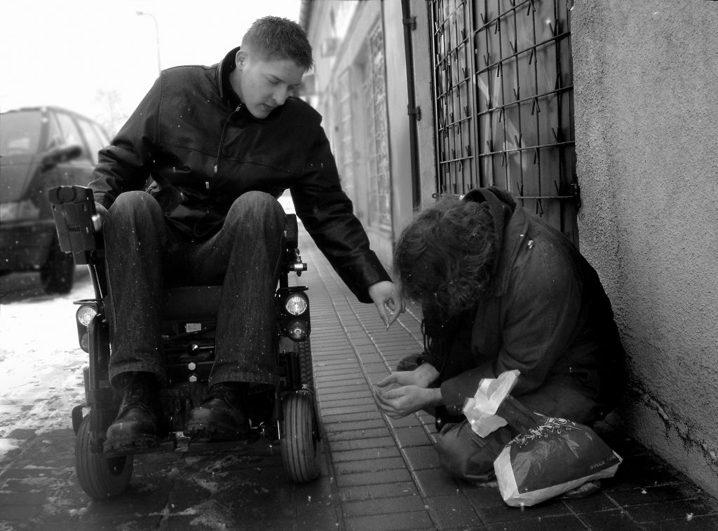 Mężczyzna na wózku daje monetę osobie, która prosi o datki na ulicy. 