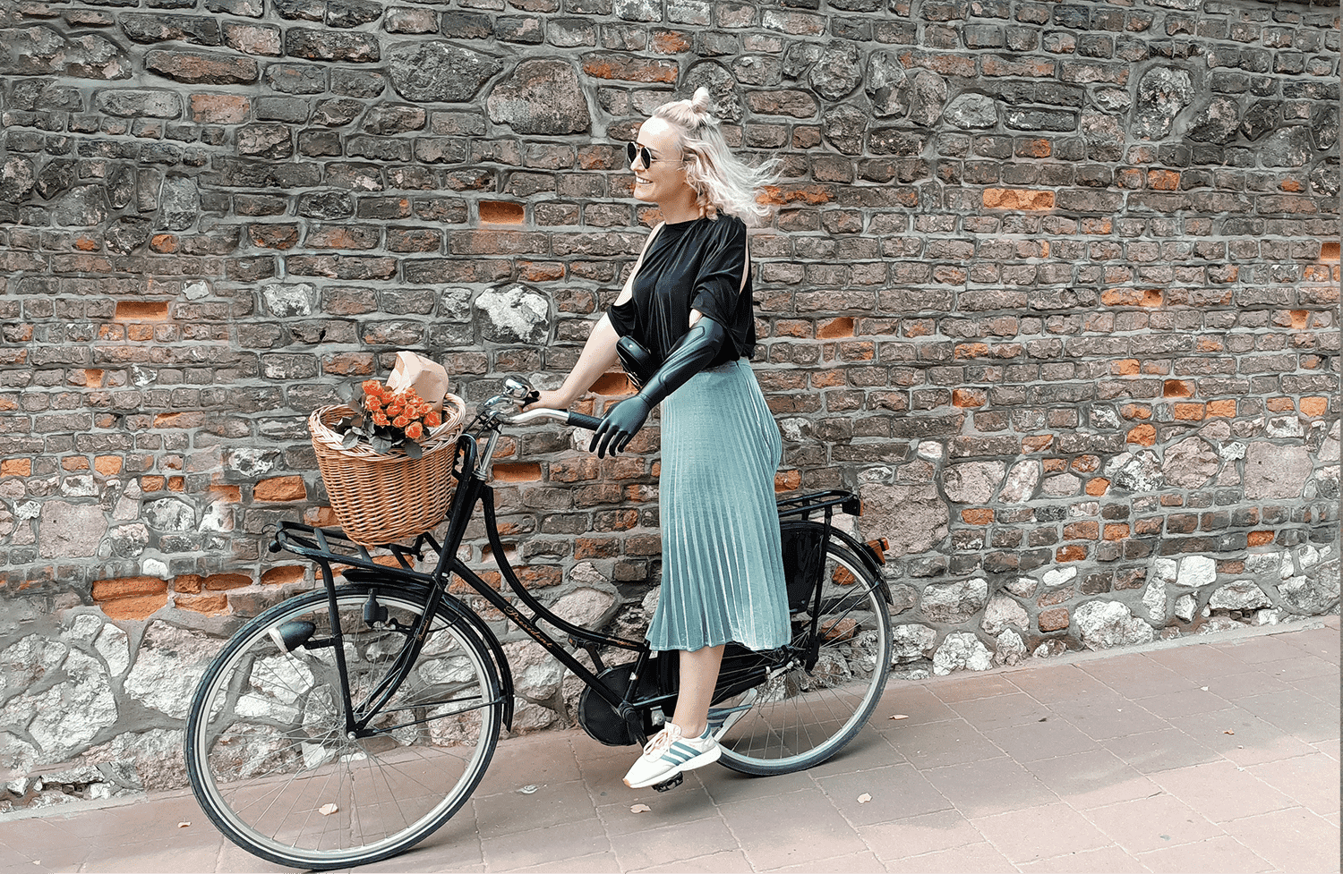 Uśmiechnięta kobieta z protezą ręki jedzie na rowerze miejskim.