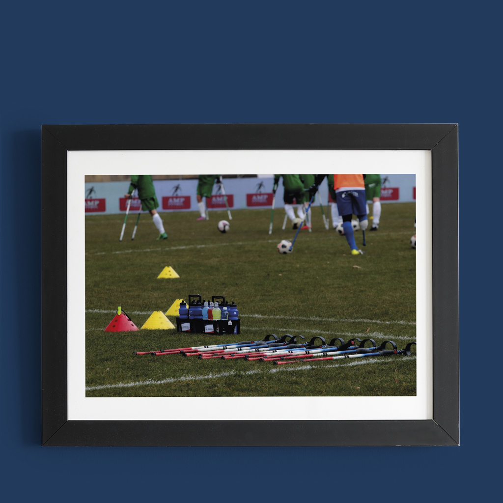 Na boisku leżą kule, w tle widać piłkarzy z amputowanymi nogami, który grają mecz.