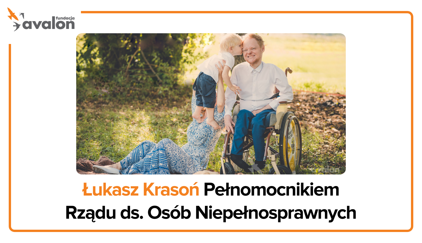 Uśmiechnięty Łukasz Krasoń na łące, jego syn stoi obok i daje mu buziaka w policzek, a obok na kocu leży jego żona.
