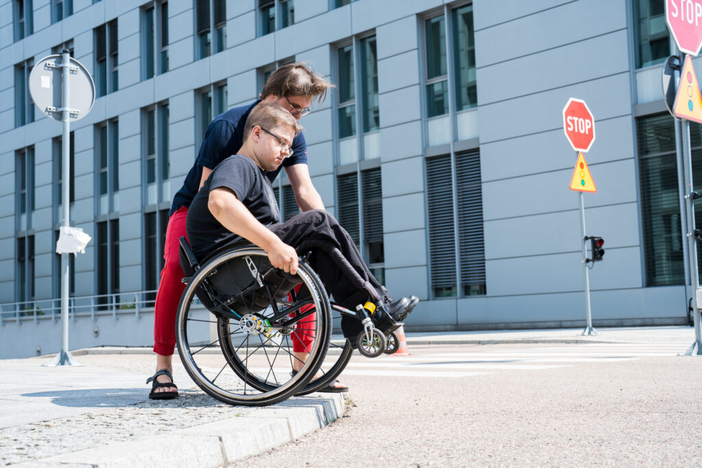 rehabilitant pomagający zjechać z krawężnika mężczyźnie na wózku inwalidzkim