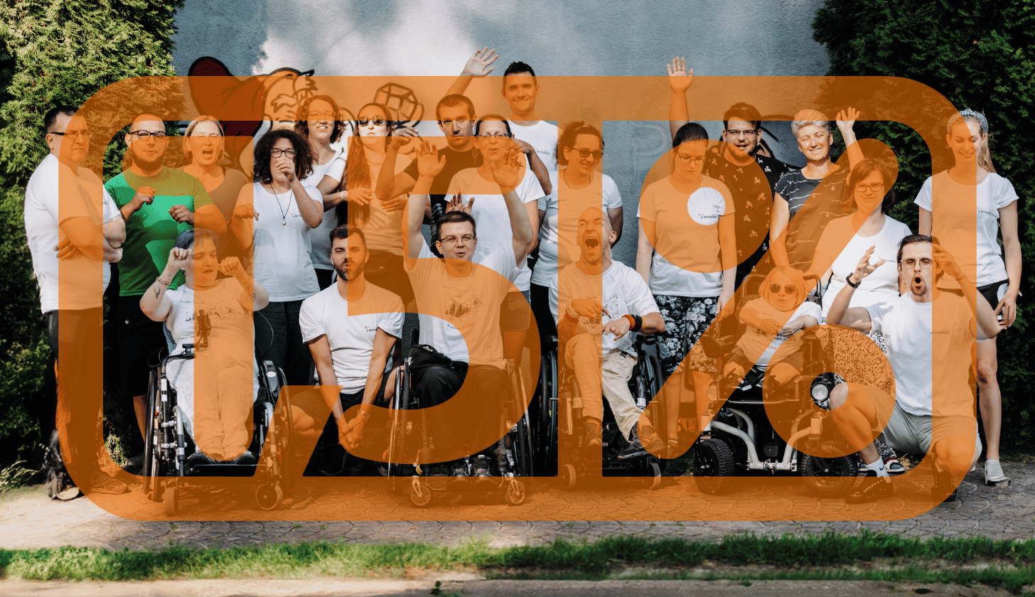 Grupowe zdjęcie osób z różnymi niepełnosprawnościami. Wszyscy uśmiechają się i mają na sobie koszulki z logotypem Fundacji Avalon.