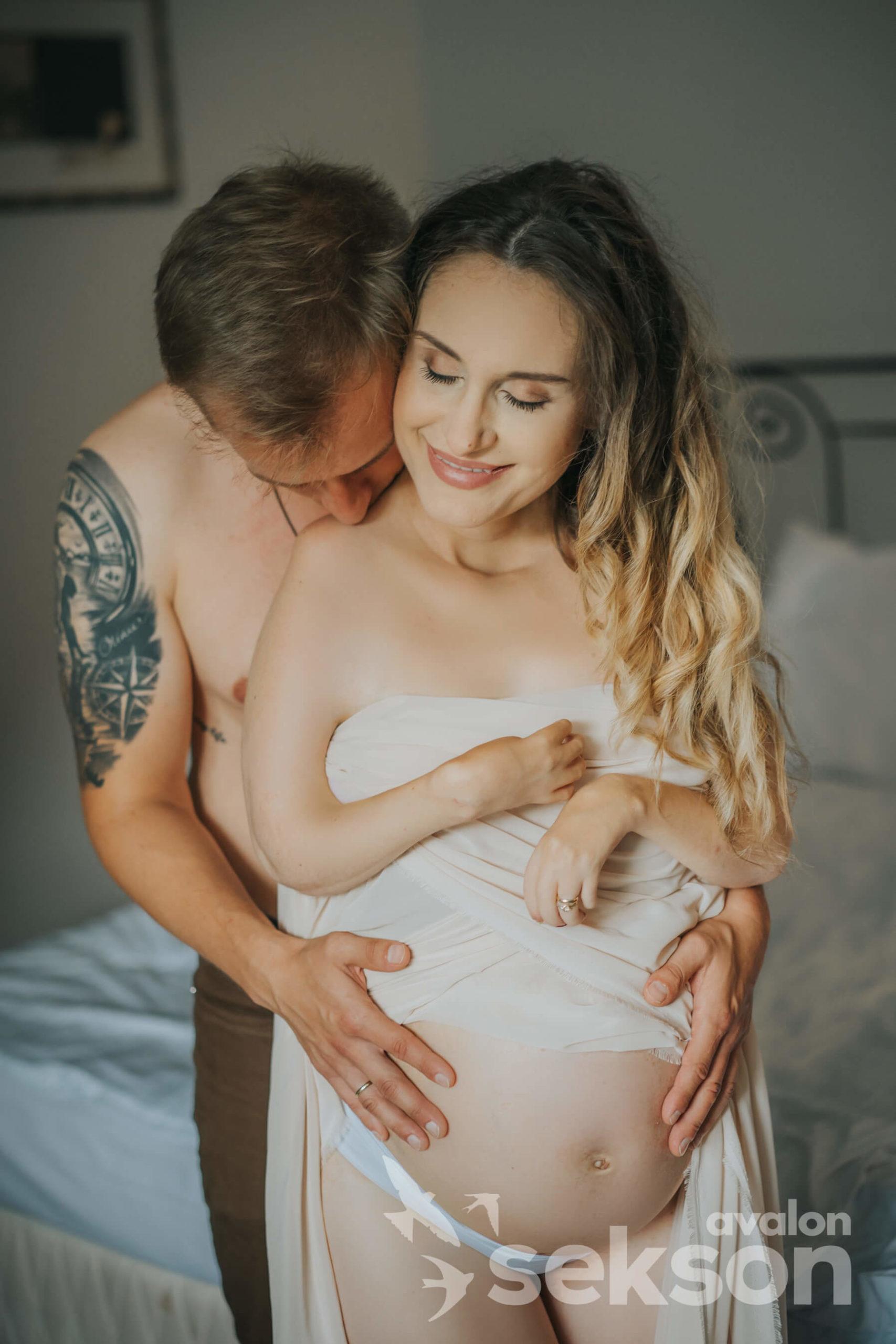 Na pierwszym planie Sylwia, za nią stoi Tomasz, obejmuję jej ciążowy brzuch i całuje ją w ramię.