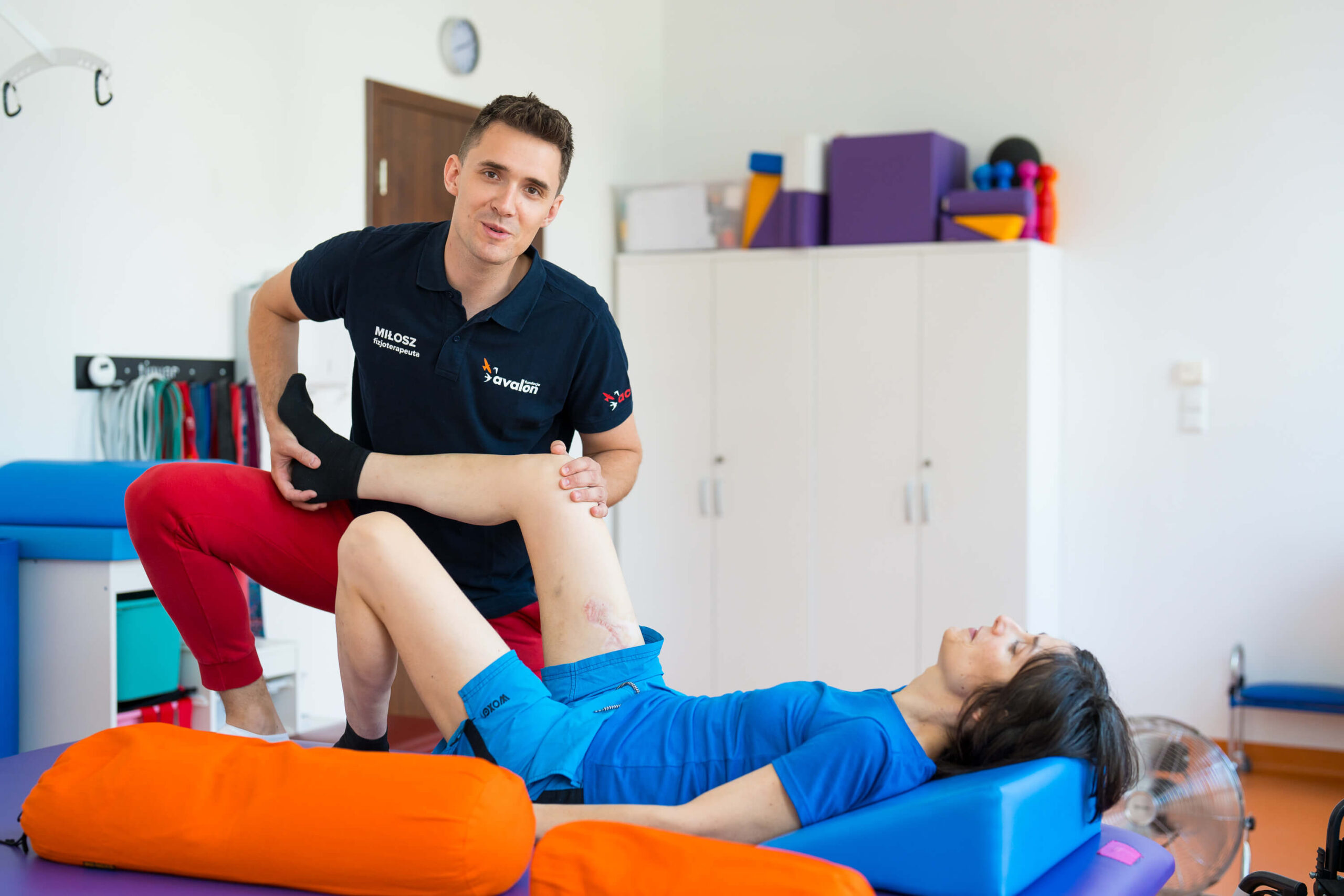 Fizjoterapeuta zgina nogę w kolanie pacjentce leżacej na leżance.