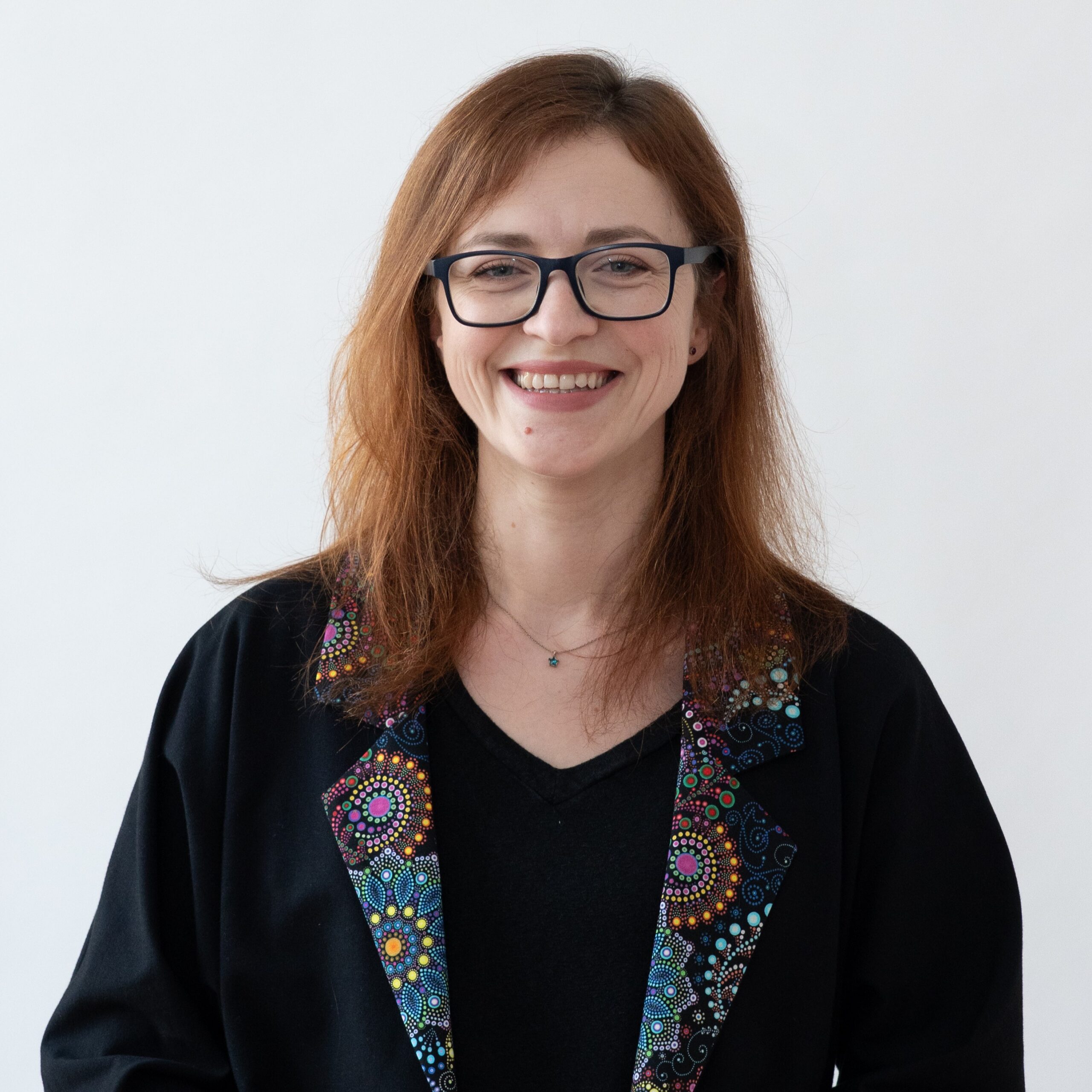 Karolina Prusińska w czarnej bluzce i czarnej marynarce z kolorowymi klapami.