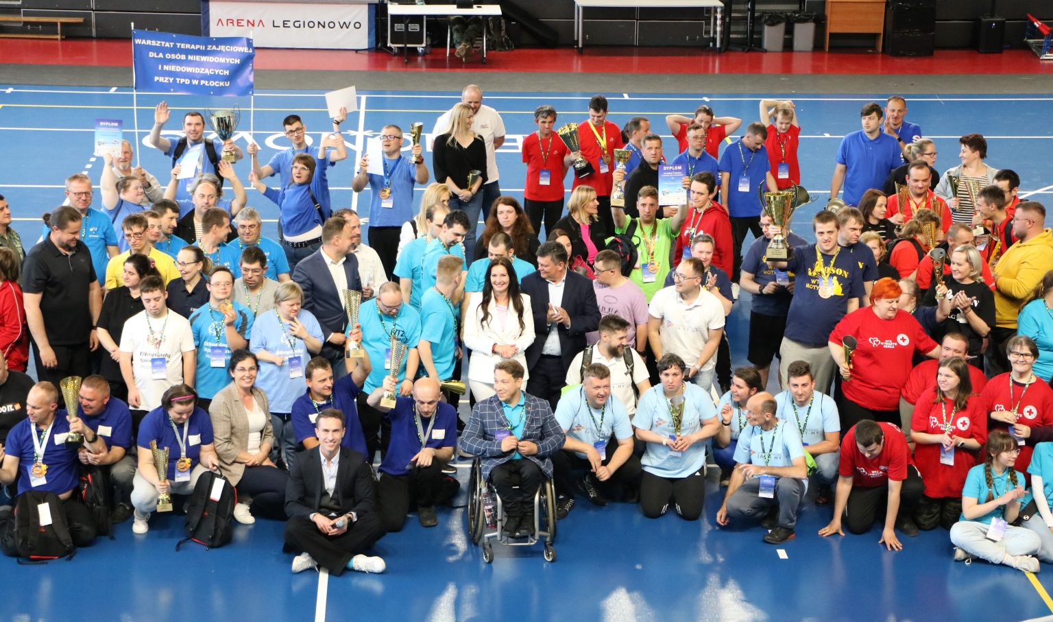 Zdjęcie grupowe uczestników wydarzenia MazONsport; w tle przestrzeń hali sportowej.