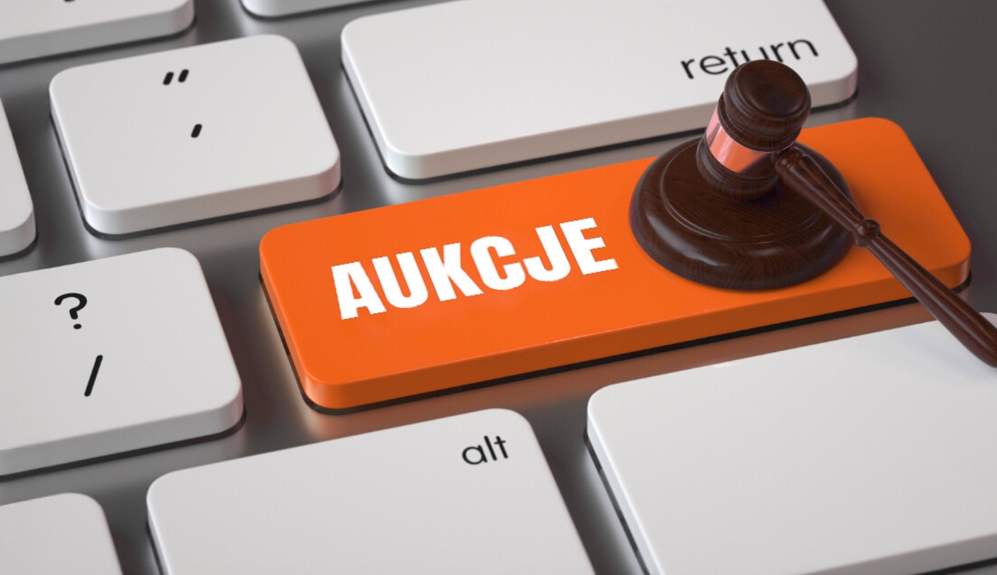 Fragment klawiatury z klawiszem z napisem aukcje, na którym leży młotek sędziowski.