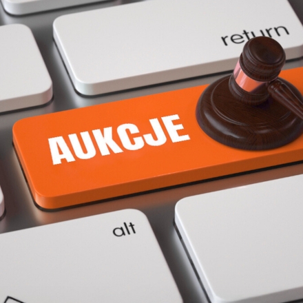 Fragment klawiatury z klawiszem z napisem aukcje, na którym leży młotek sędziowski.