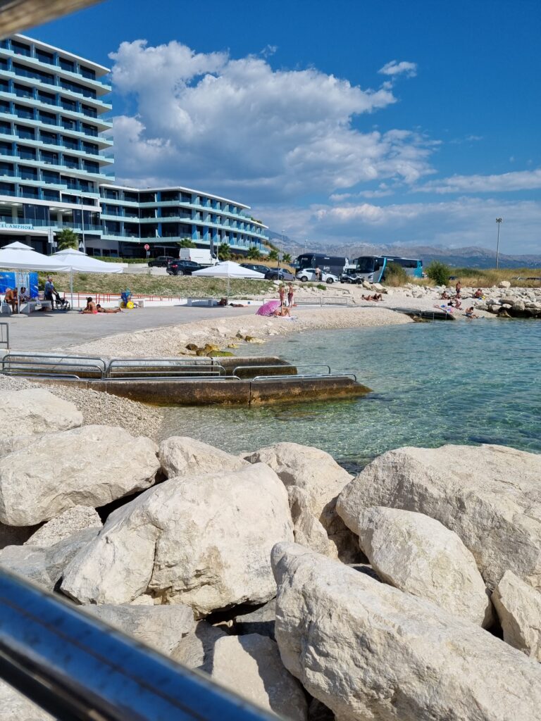 Kamienna plaża i zjazd do wody. W tle budynki.