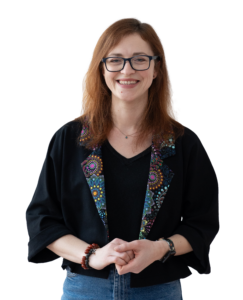 Zdjęcie Karoliny Prusińskiej od pasa w górę. Ma na sobie czarną marynarkę z rękawami 3/4 i kolorowymi klapami, czarną bluzkę i okulary.