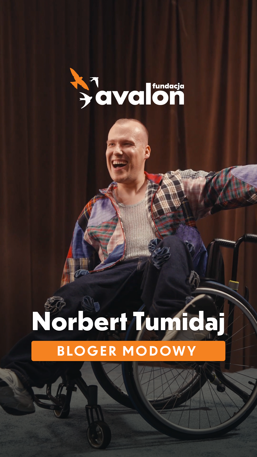 Uśmiechnięty Norbert na wózku w kolorowej marynarce. Napis: Norbert Tumidaj Bloger modowy