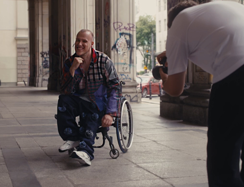 Uśmiechniety Norbert pozuje do zdjęcia. Z prawej strony pochylony fotograf.