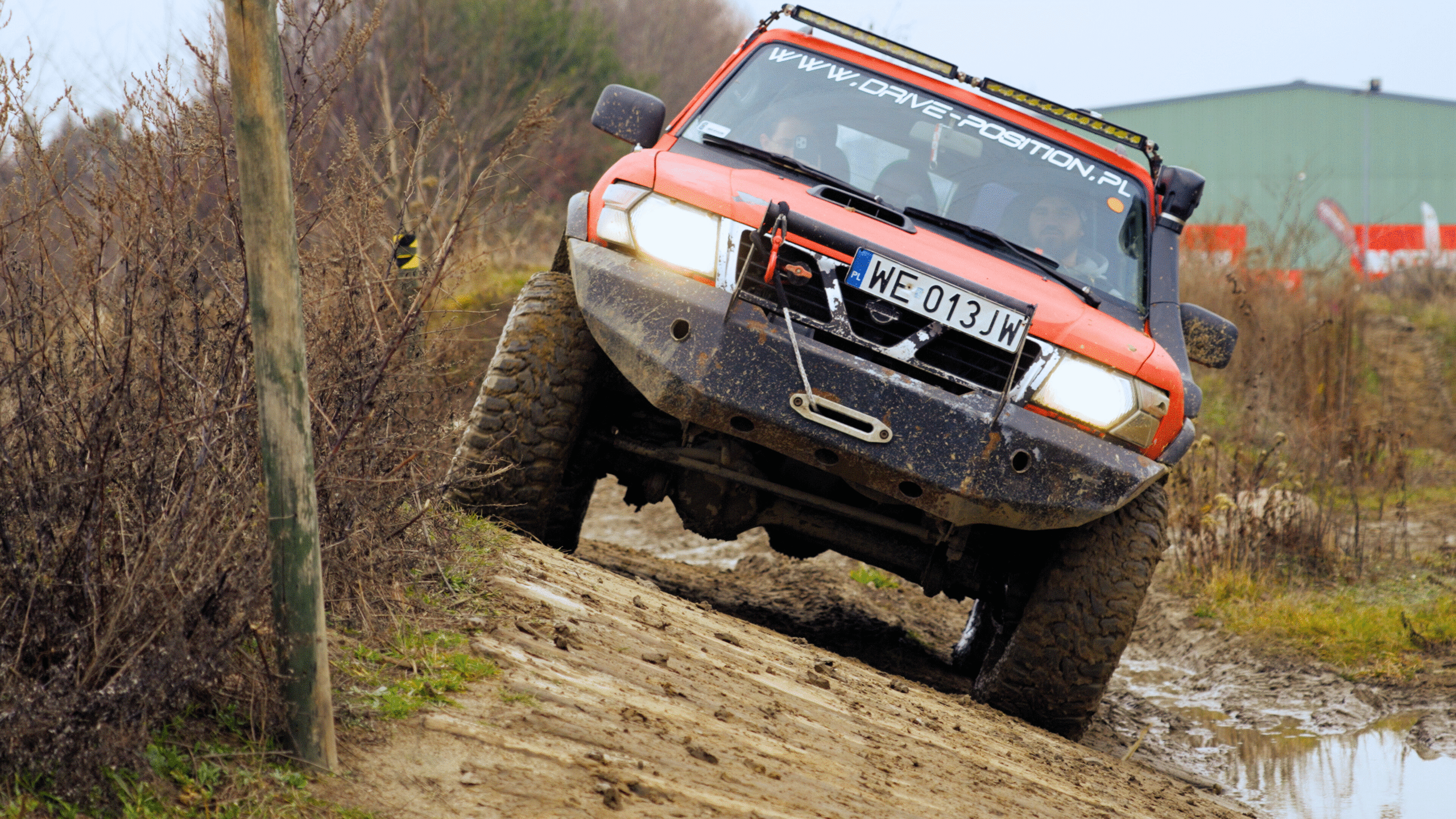 Samochód 4x4 podczas przejazdu po pochyłej drodze, przechylony w prawo o ok. 30 stopni. w tle tor drive position moto sport.