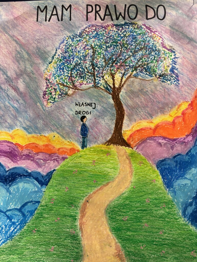 Na rysunku drzewo na wzgórzu. Pod drzewem stoi postać. Nad drzewem napis Mam prawo do własnej drogi. Wokół wzgórza kolorowe chmury.