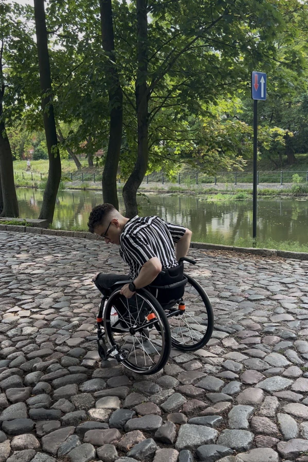 Mężczyzna na wózku próbuje pokonać wybrukowany chodnik.