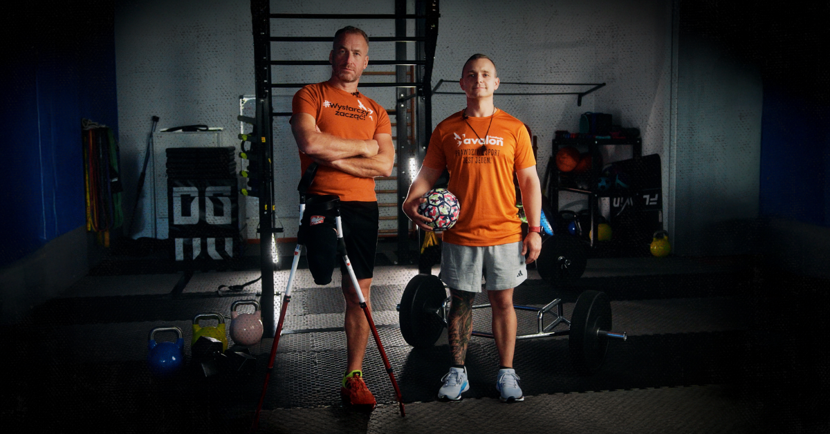 dwóch mężczyzn ubranych w sportowe stroje pozuje do zdjęcia, w tle sala treningowa
