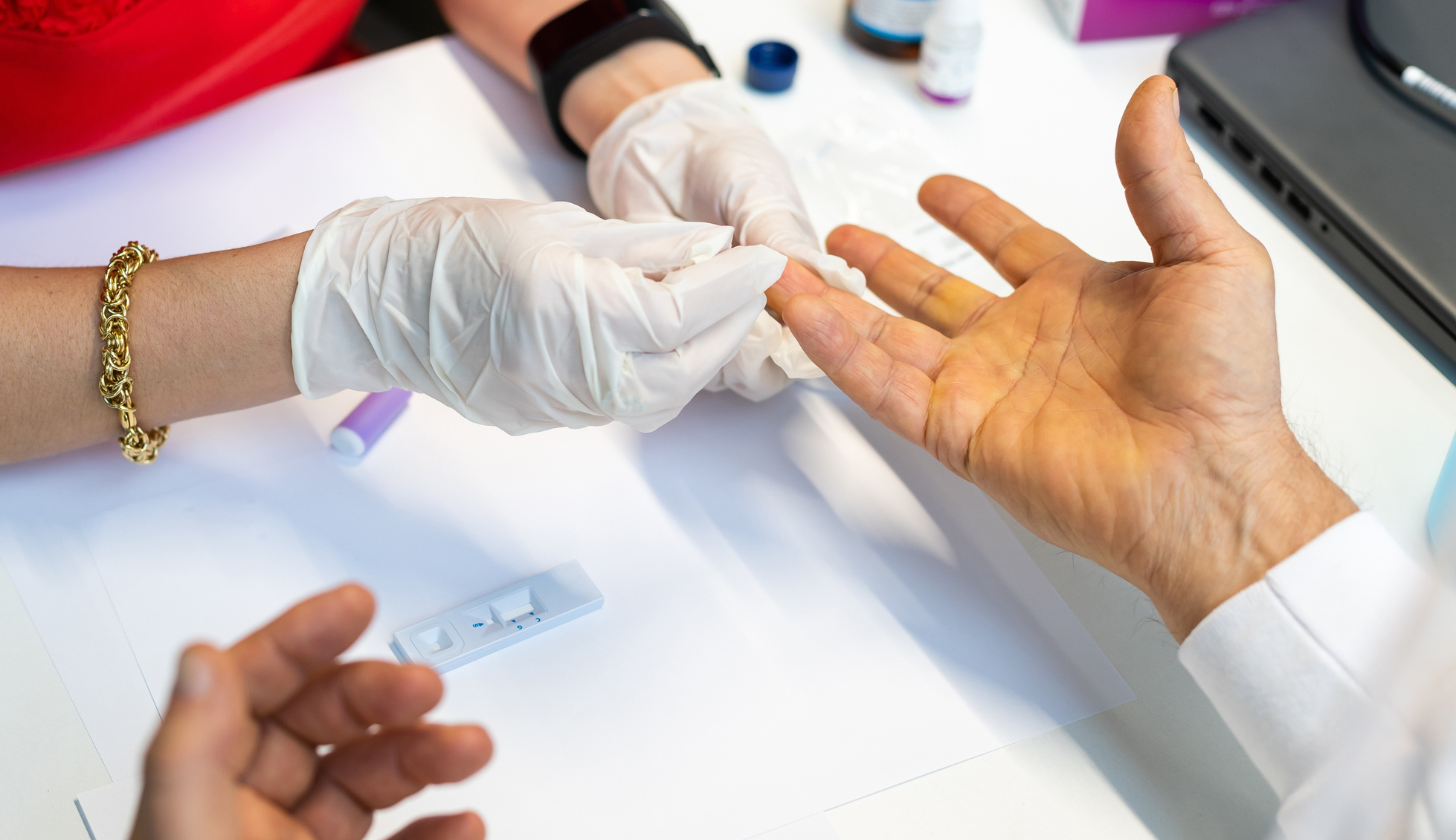 grafika promująca bezpłatne testy w Fundacji Avalon. Widać dłonie w jednorazowych rękawiczkach pobierające krew z palca drugiej osoby