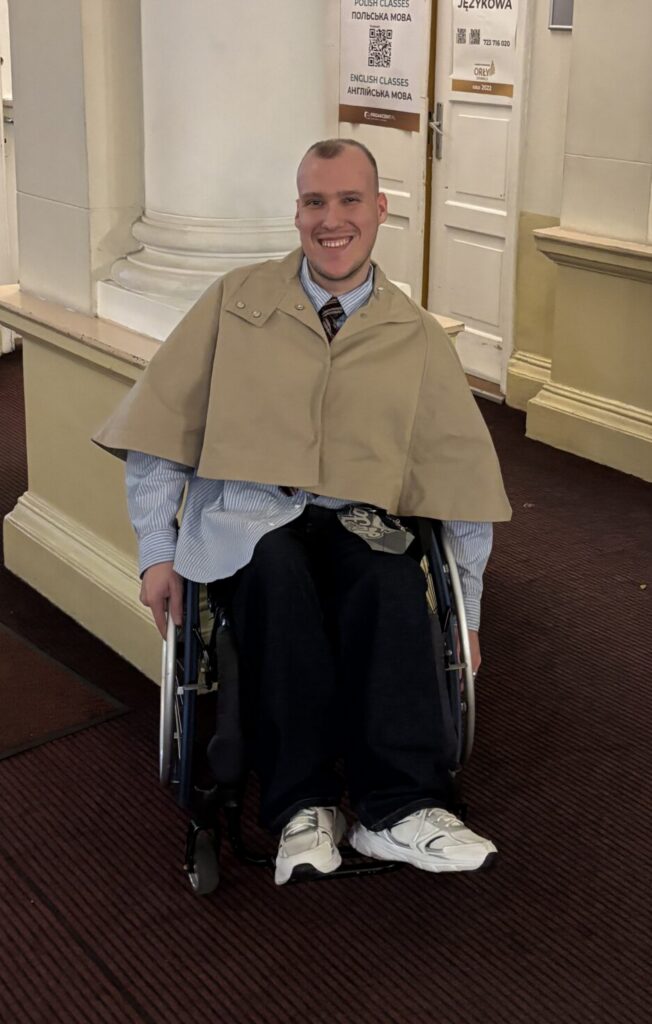 Norbert Tumidaj na wózku w zarzuconej na ramiona pelerynie.