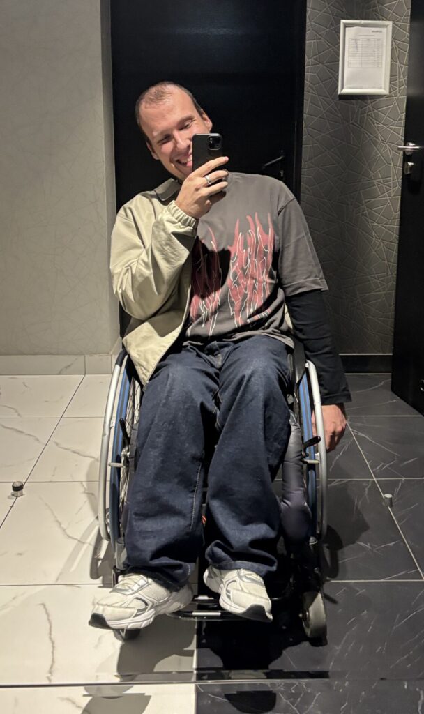 Norbert Tumidaj na wózku w dżinsowych spodniach i t-shrcie z nadrukiem.