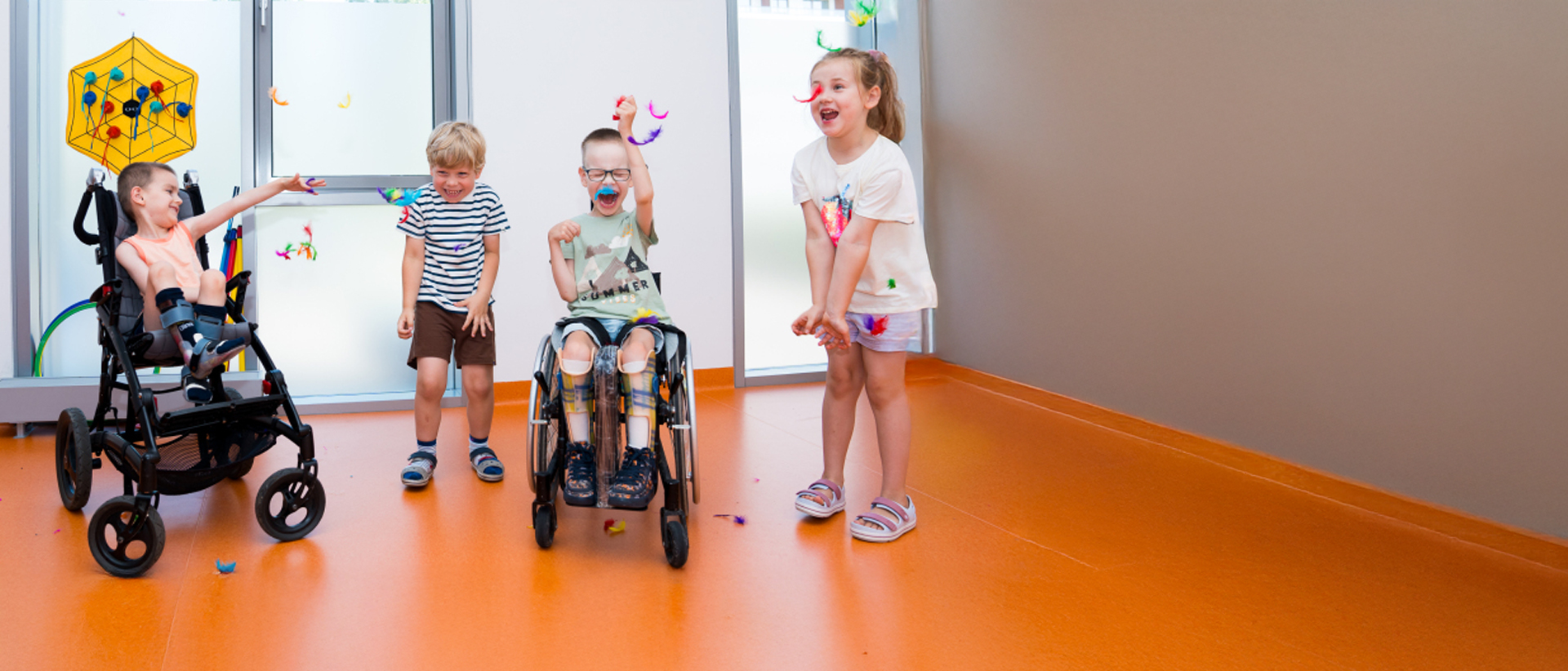 Na zdjęciu 4 dzieci, dwoje z nich na wózkach, bawią się na sali rehabilitacyjnej.