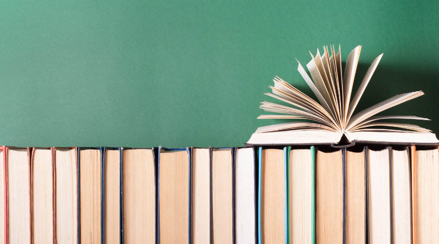 Książki ustawione w szergu. Na nich lezy jedna otwarta ksiązka.