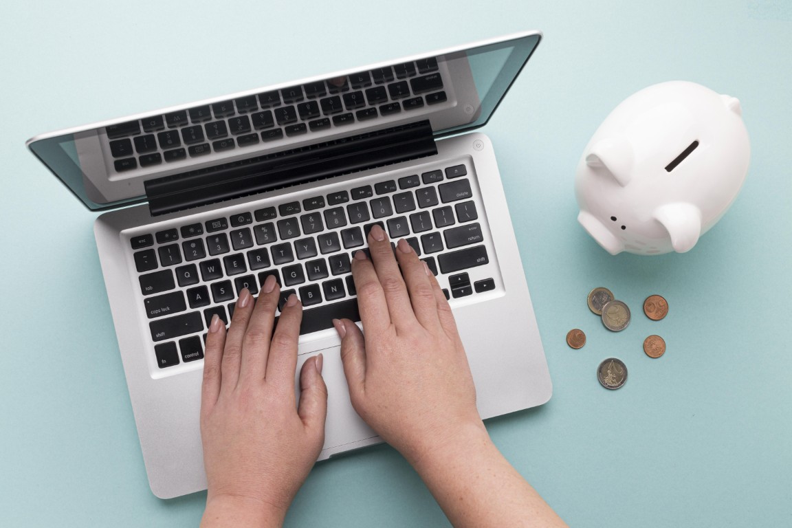 Osoba pracuje na laptopie, obok którego stoi skarbonka