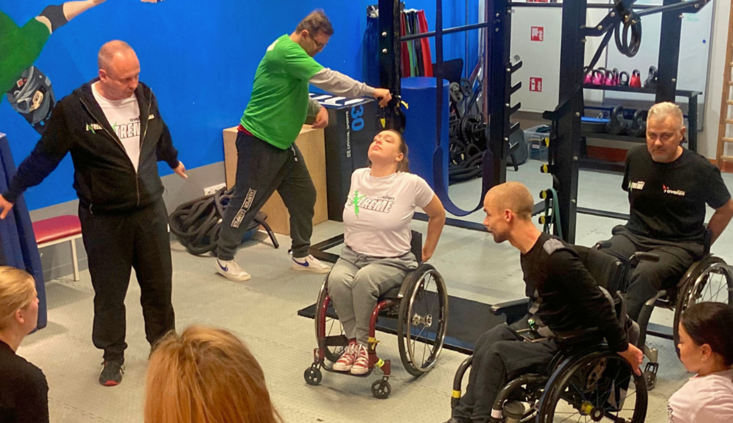 grupa osób z niepełnosprawnościami ćwiczy w sali treningowej pod okiem trenera