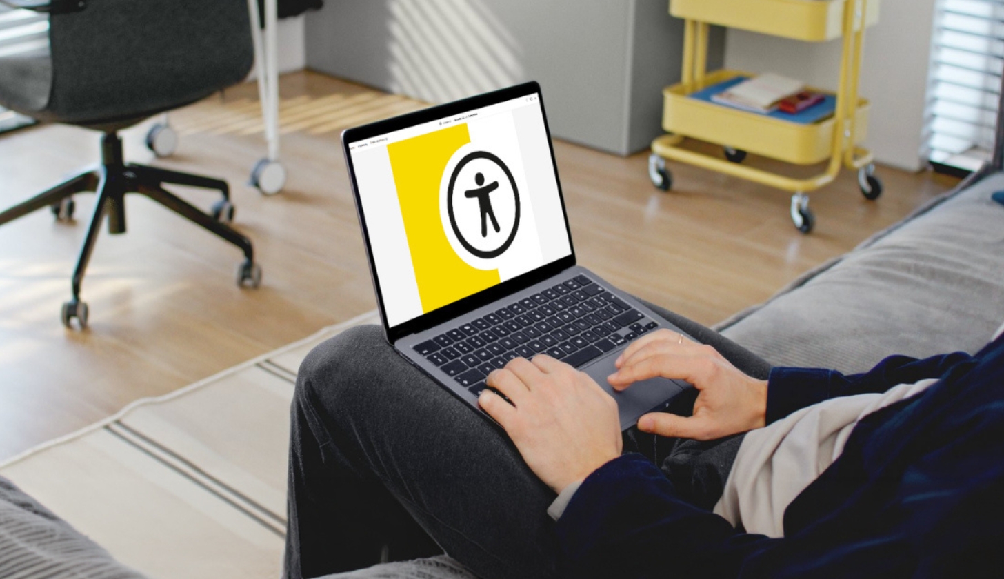 W pokoju mężczyzna siedzi i trzyma na kolanach laptop. Na ekranie widać logo broszury pfron.