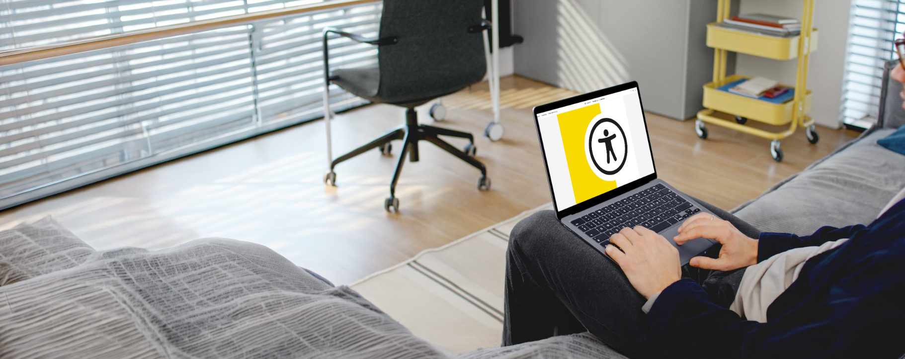 W pokoju mężczyzna siedzi i trzyma na kolanach laptop. Na ekranie widać logo broszury pfron.