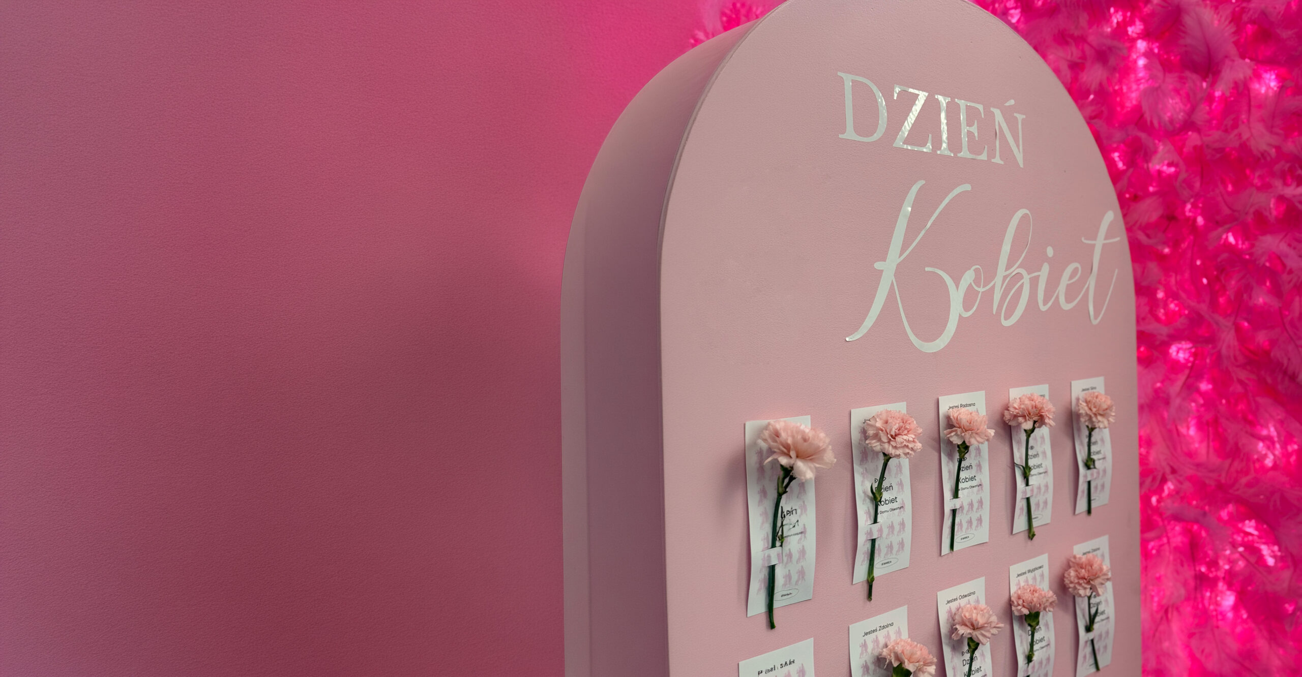 Napis dzień kobiet i przymocowane pojedyncze różowe kwiatki do różowej planszy.
