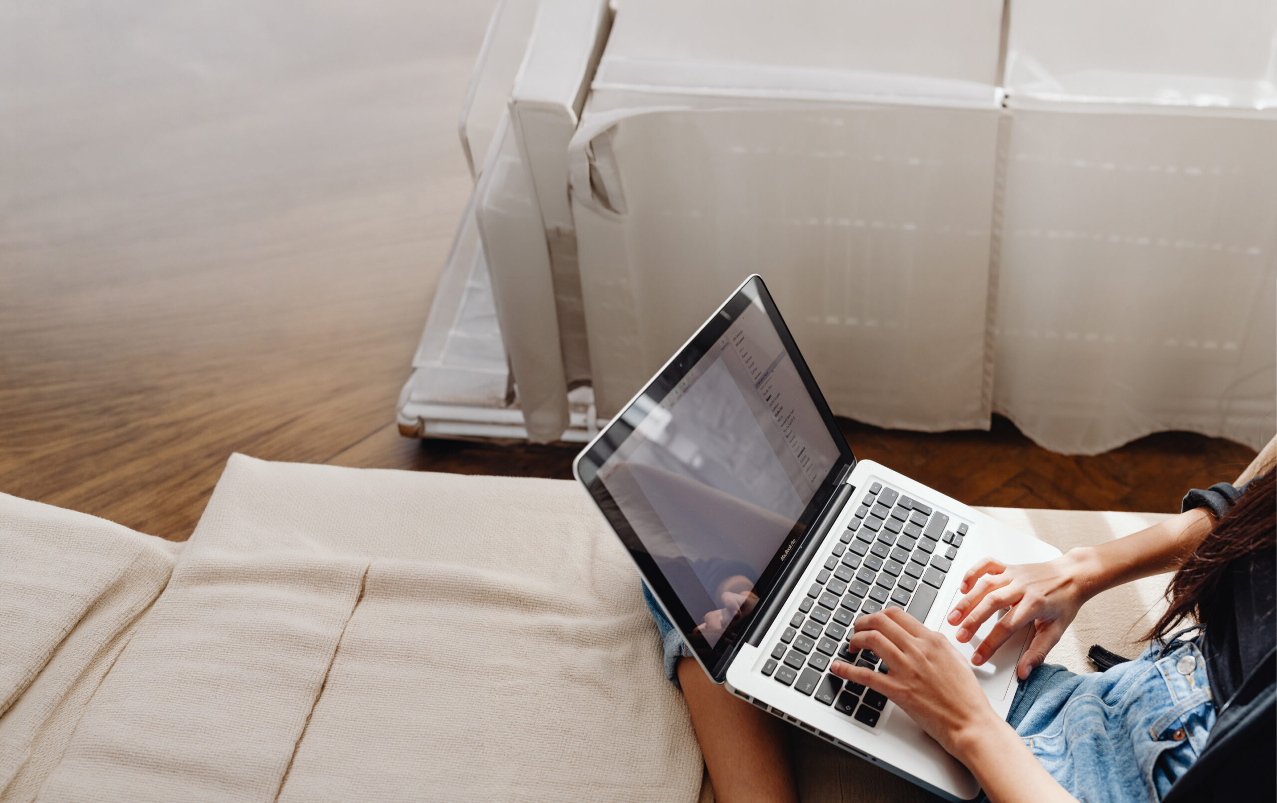 Osoba siedzi w pokoju trzymając laptop na kolanach.