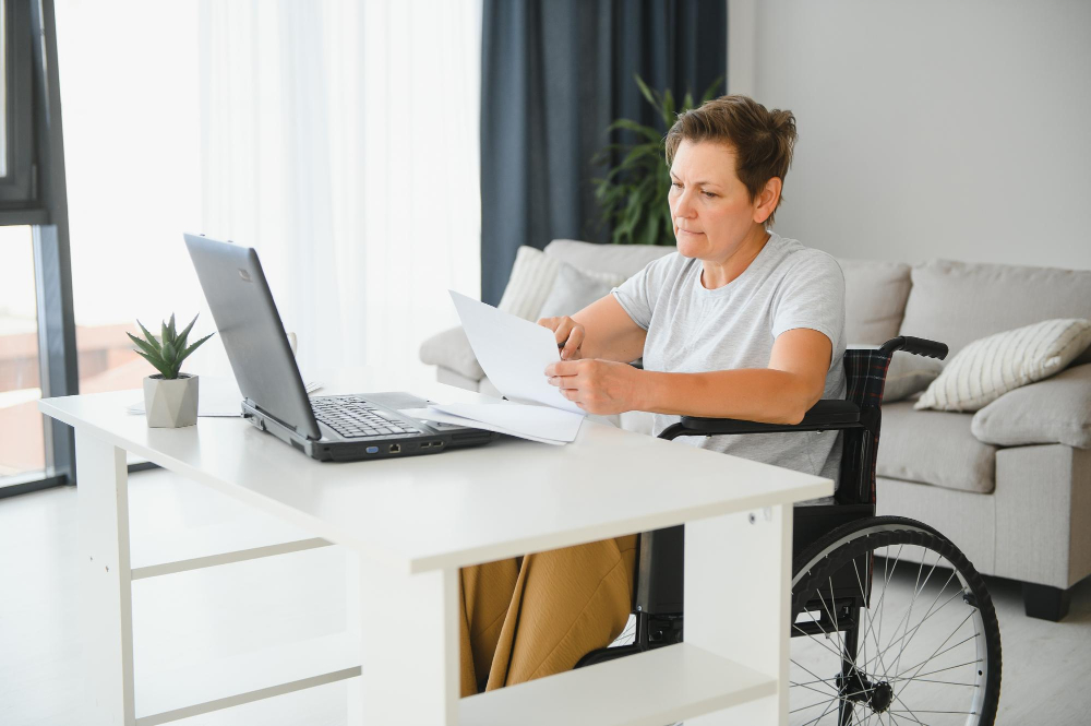kobieta na wózku inwalidzkim składa dokumenty online na laptopie