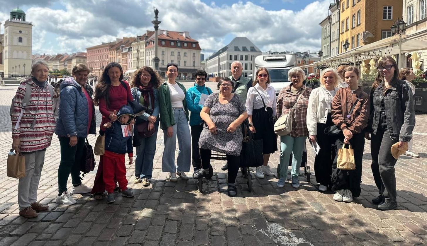 Grupa kobiet i jeden mężczyzna stojących obok siebie na ulicy Starego Miasta w Warszawie. W tle kolorowe kamienice.