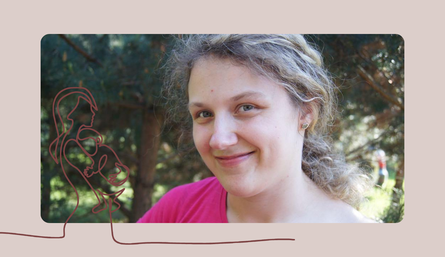 Portret uśmiechniętej osoby z krótkimi, jasnobrązowymi włosami, ubranej w różową bluzkę. Osoba patrzy w obiektyw, a w tle widać rozmyte drzewa i zieleń w słoneczny dzień.