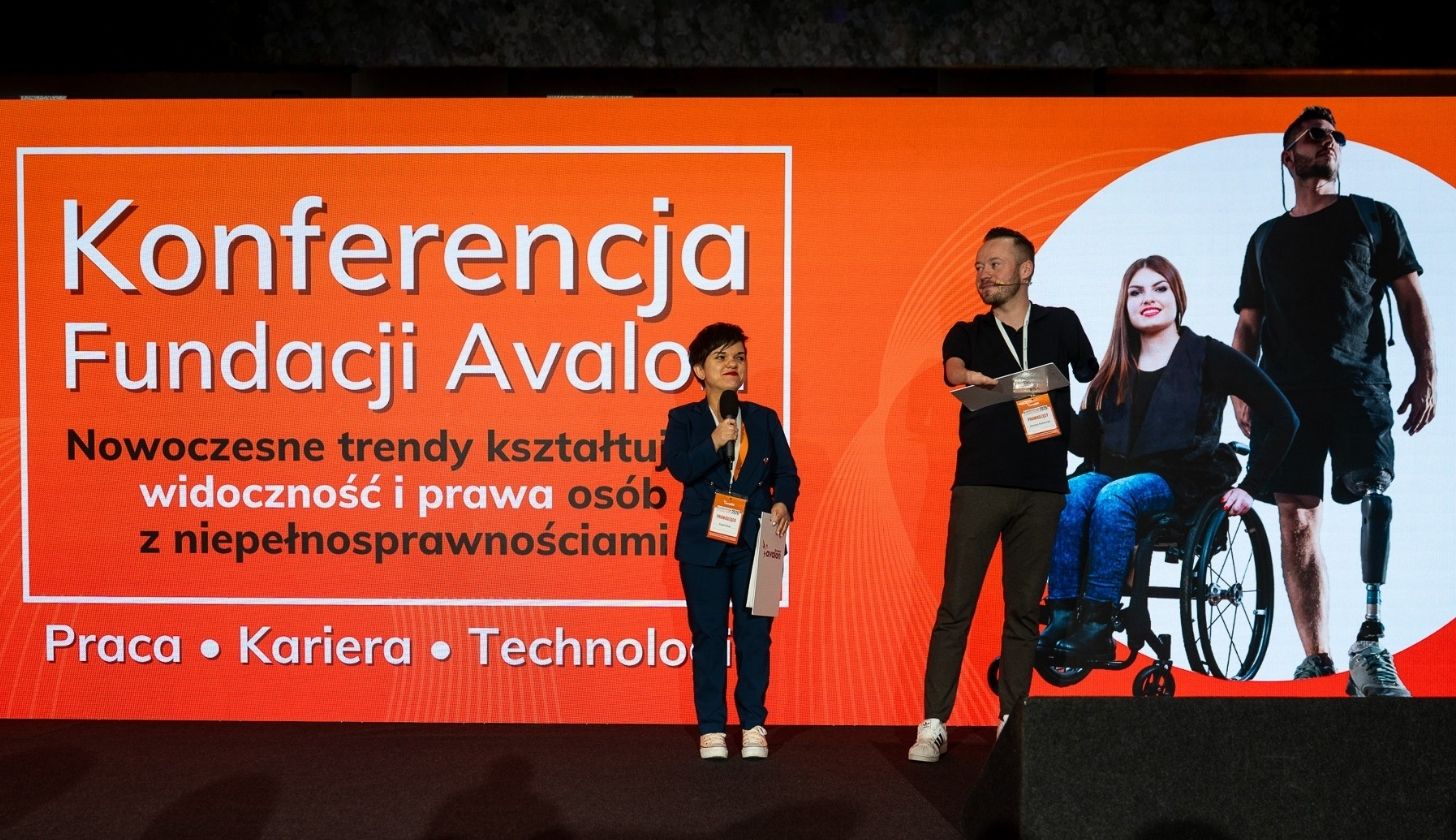 Kobieta i mężczyzna mówią przez mikrofony w tle logo konferencji.