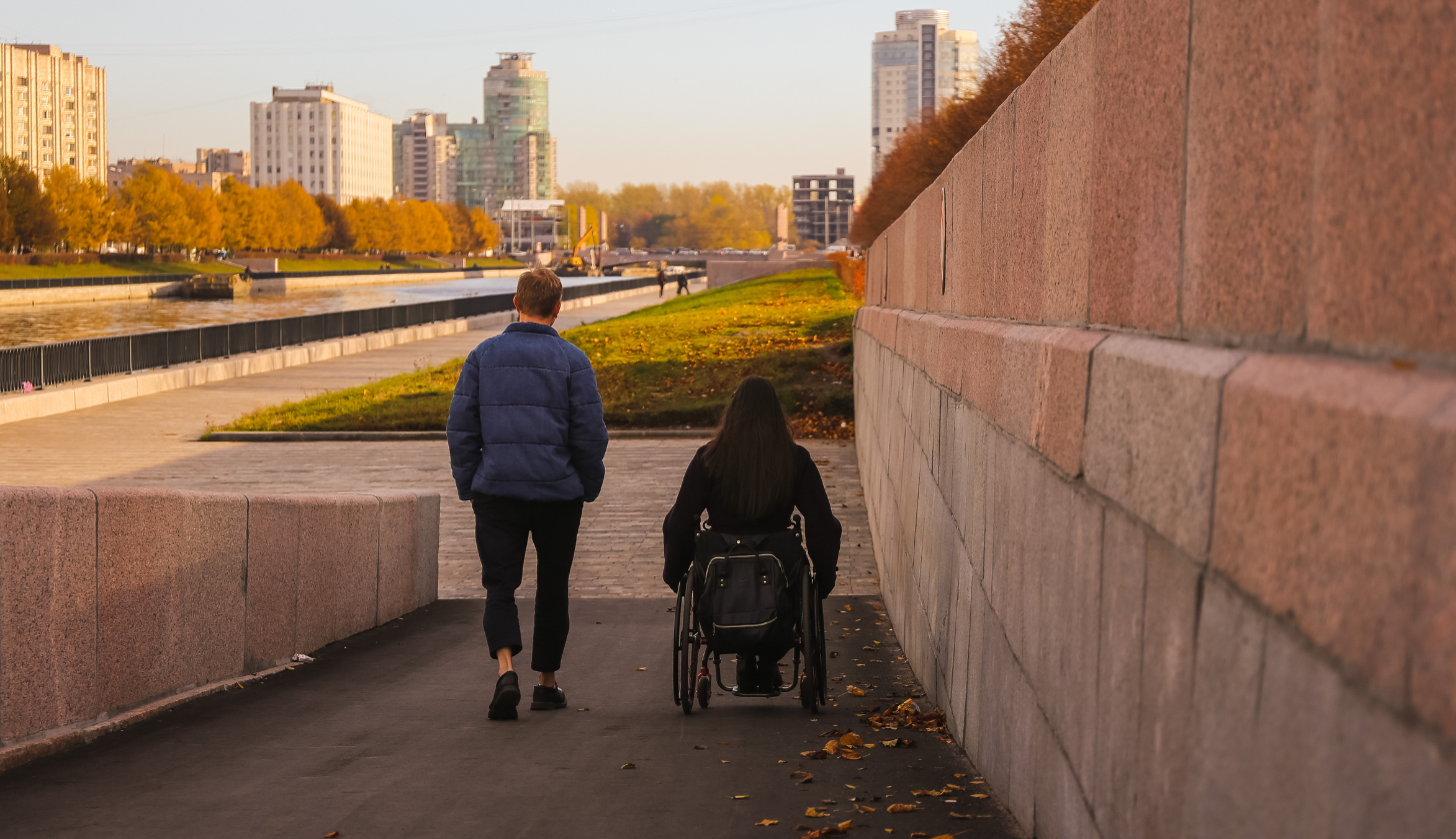 mężczyzna oraz kobieta poruszająca się na wózku idą obok siebie na jesiennym spacerze
